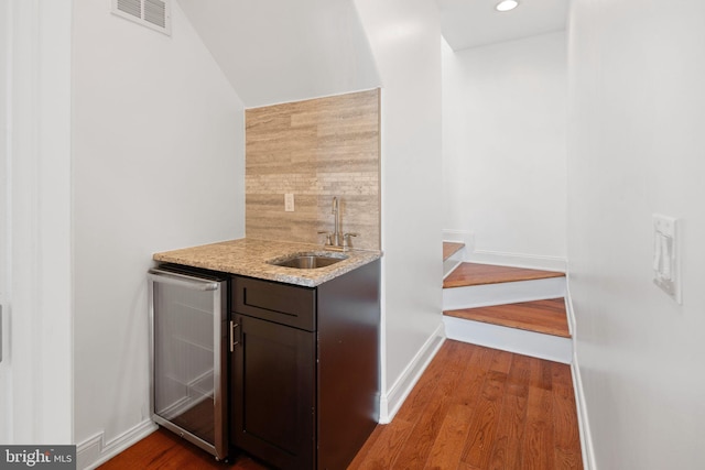 bar with dark brown cabinetry, beverage cooler, sink, and wood-type flooring