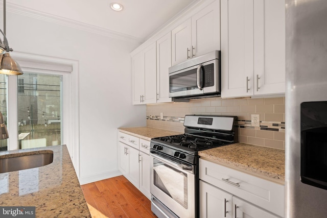 kitchen featuring appliances with stainless steel finishes, decorative light fixtures, white cabinetry, and light hardwood / wood-style flooring