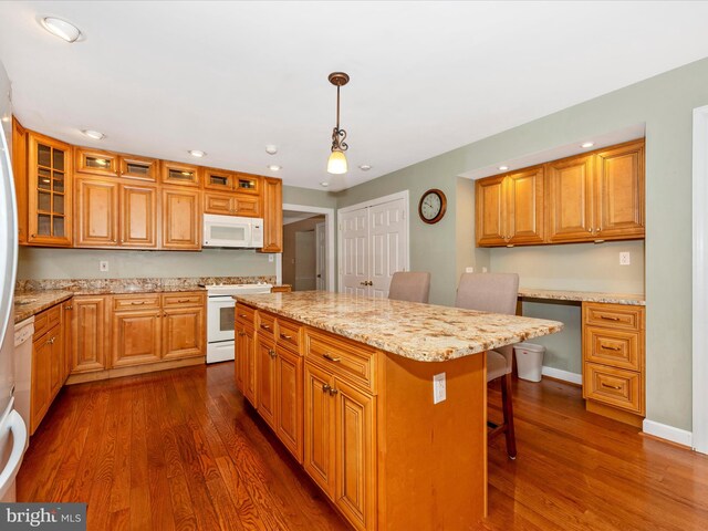 kitchen with white appliances, decorative light fixtures, dark hardwood / wood-style floors, a center island, and a breakfast bar area