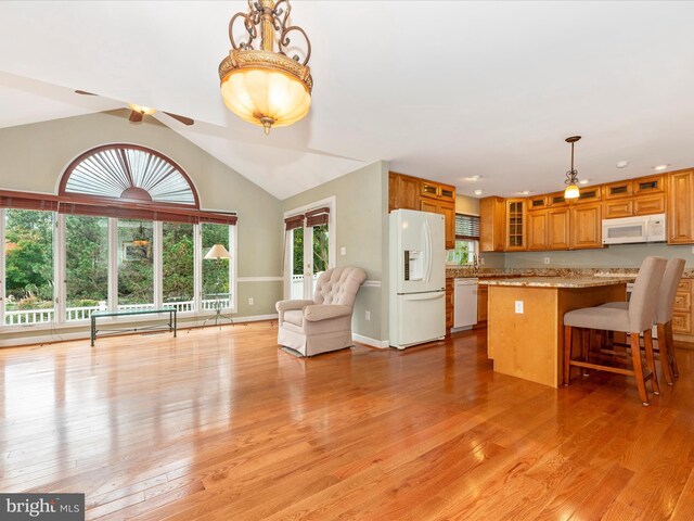 kitchen with pendant lighting, white appliances, vaulted ceiling, and light hardwood / wood-style floors