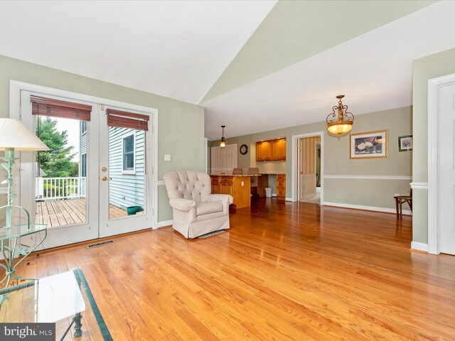 unfurnished living room with french doors, light wood-type flooring, a chandelier, and vaulted ceiling