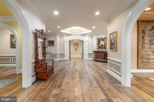 hall with wood-type flooring, ornamental molding, and a notable chandelier