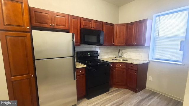 kitchen featuring black appliances, sink, light hardwood / wood-style flooring, decorative backsplash, and light stone counters