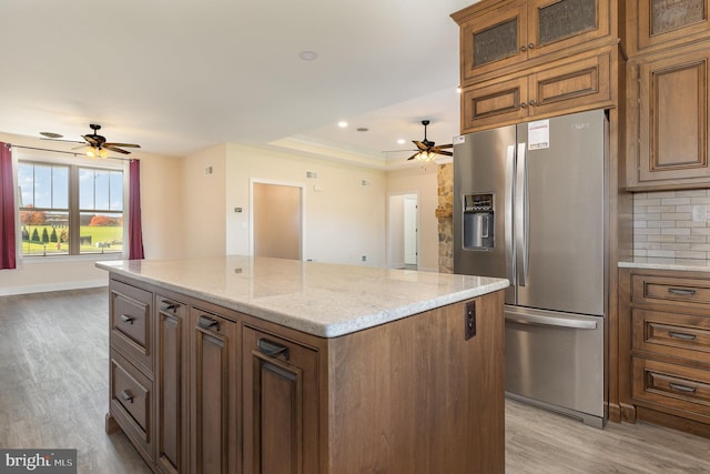 kitchen featuring light stone countertops, backsplash, a center island, light hardwood / wood-style floors, and stainless steel refrigerator with ice dispenser