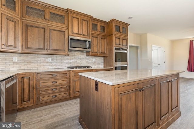 kitchen with backsplash, appliances with stainless steel finishes, light stone countertops, light hardwood / wood-style floors, and a center island