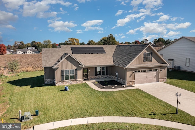 view of front of house with central air condition unit, solar panels, a front yard, and a garage