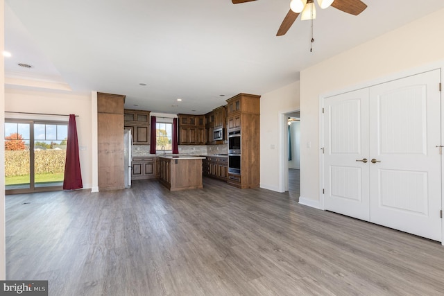 kitchen with a kitchen island, light hardwood / wood-style flooring, backsplash, appliances with stainless steel finishes, and ceiling fan