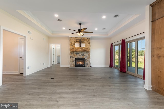 unfurnished living room with a fireplace, a raised ceiling, hardwood / wood-style floors, ceiling fan, and ornamental molding