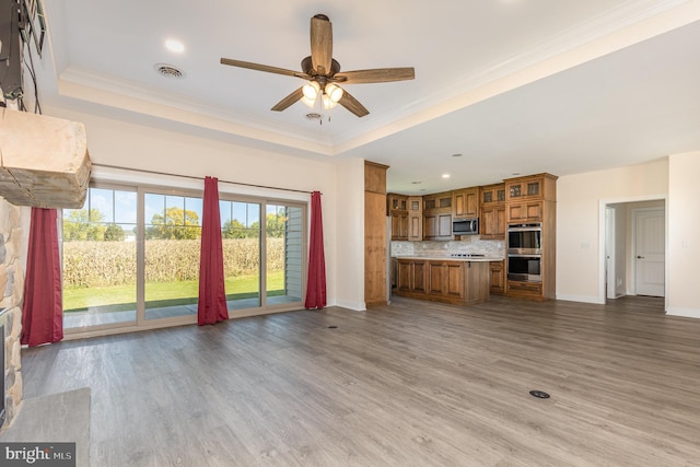 unfurnished living room with ornamental molding, ceiling fan, a tray ceiling, and hardwood / wood-style flooring