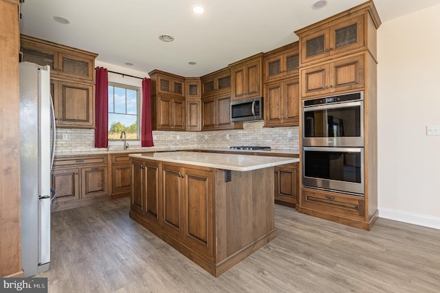 kitchen with decorative backsplash, appliances with stainless steel finishes, light hardwood / wood-style flooring, sink, and a center island