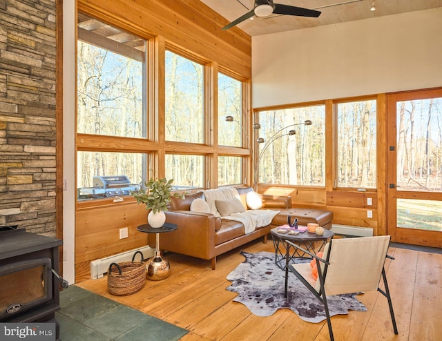 sunroom / solarium with a wood stove, a wealth of natural light, ceiling fan, and a baseboard radiator