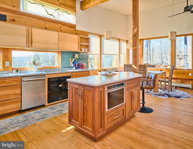 kitchen featuring a center island, stainless steel appliances, beamed ceiling, decorative light fixtures, and light wood-type flooring