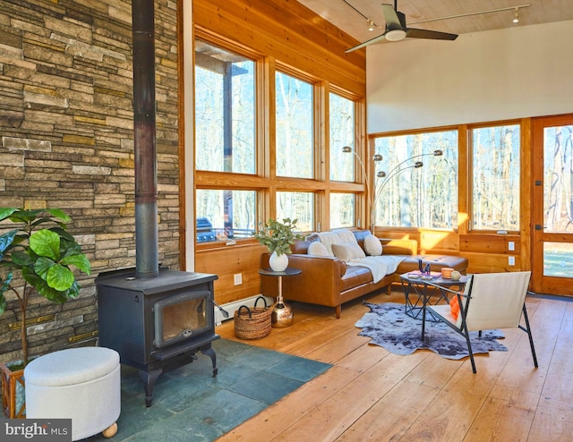 sunroom / solarium with a baseboard radiator, a wood stove, and ceiling fan