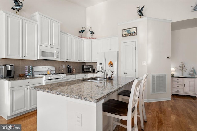 kitchen featuring wood-type flooring, sink, an island with sink, white cabinets, and white appliances