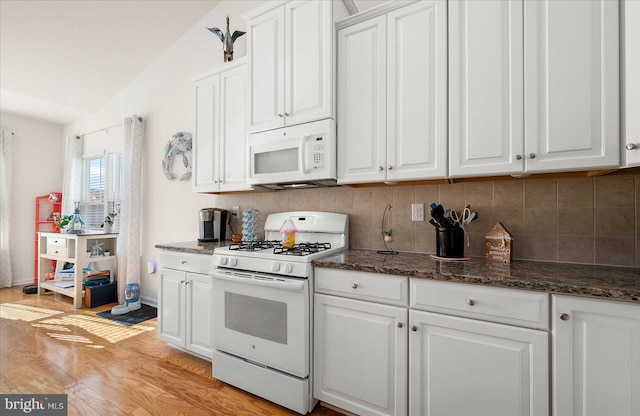 kitchen with white cabinetry, dark stone counters, white appliances, light hardwood / wood-style flooring, and vaulted ceiling