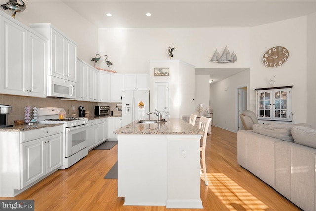 kitchen with white cabinets, light wood-type flooring, white appliances, and an island with sink