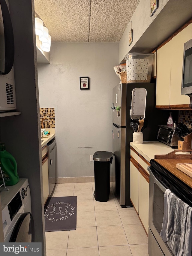 kitchen with washer / dryer, stainless steel appliances, white cabinets, tasteful backsplash, and light tile patterned floors