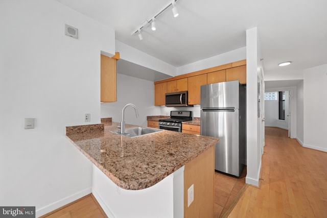 kitchen with kitchen peninsula, rail lighting, light hardwood / wood-style flooring, sink, and stainless steel appliances