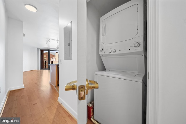 laundry area with electric panel, stacked washer and dryer, and light hardwood / wood-style flooring