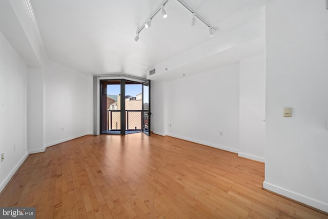 empty room with vaulted ceiling, light wood-type flooring, and rail lighting