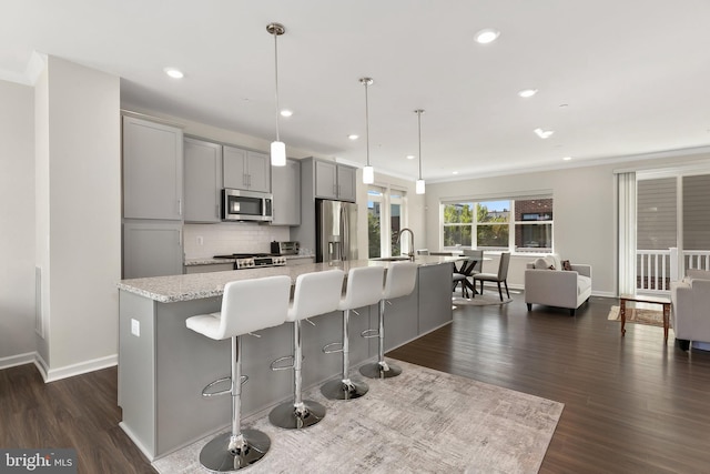 kitchen featuring hanging light fixtures, an island with sink, appliances with stainless steel finishes, light stone countertops, and gray cabinets