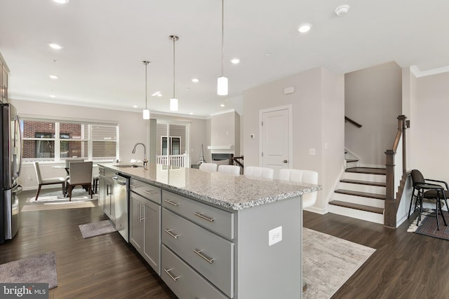 kitchen with appliances with stainless steel finishes, pendant lighting, dark hardwood / wood-style floors, and a kitchen island with sink