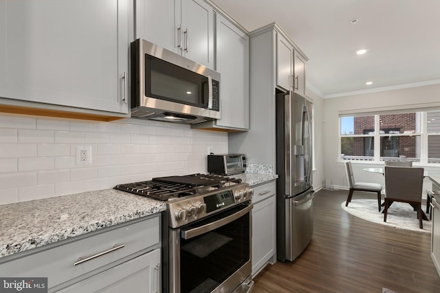 kitchen with dark wood-type flooring, light stone counters, appliances with stainless steel finishes, and ornamental molding