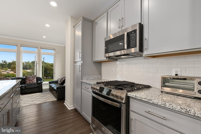 kitchen featuring light stone counters, dark hardwood / wood-style flooring, gray cabinets, crown molding, and stainless steel appliances