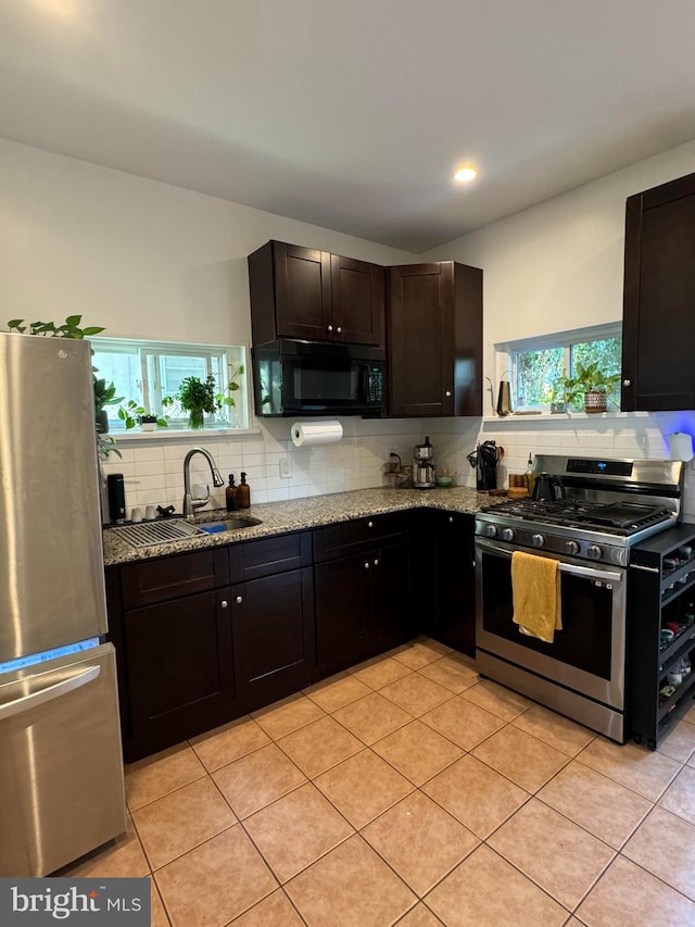 kitchen featuring sink, light tile patterned floors, appliances with stainless steel finishes, dark brown cabinets, and light stone counters