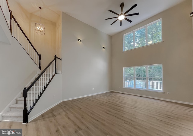 unfurnished living room featuring light hardwood / wood-style flooring, high vaulted ceiling, ceiling fan with notable chandelier, and a wealth of natural light