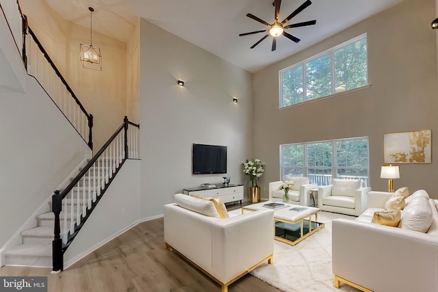 living room with hardwood / wood-style floors, ceiling fan with notable chandelier, and a high ceiling