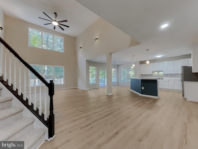 unfurnished living room featuring light hardwood / wood-style flooring, ceiling fan with notable chandelier, and high vaulted ceiling