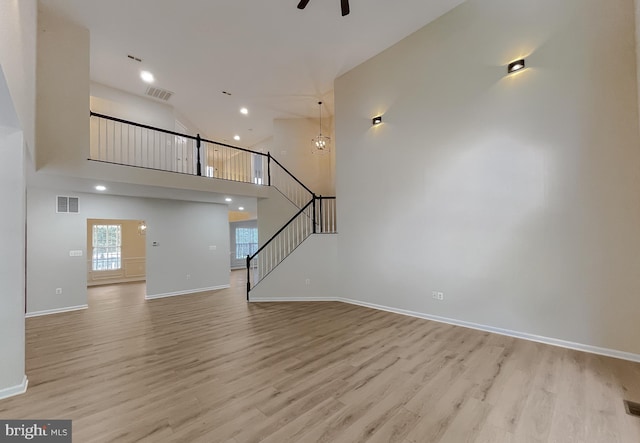 unfurnished living room featuring ceiling fan, a high ceiling, and light wood-type flooring