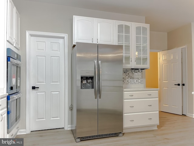 kitchen featuring white cabinetry, stainless steel appliances, decorative backsplash, and light wood-type flooring