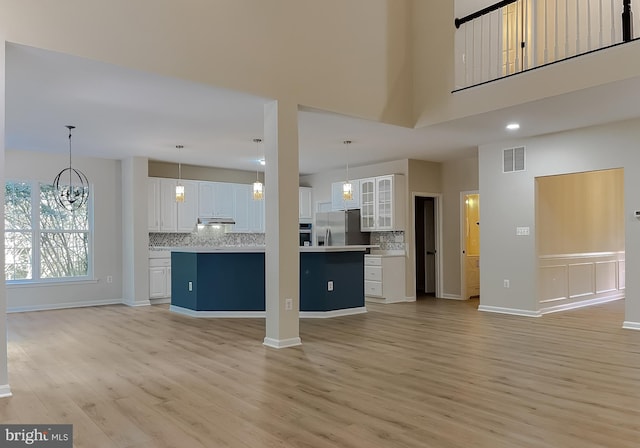 unfurnished living room with a notable chandelier, a towering ceiling, and light wood-type flooring