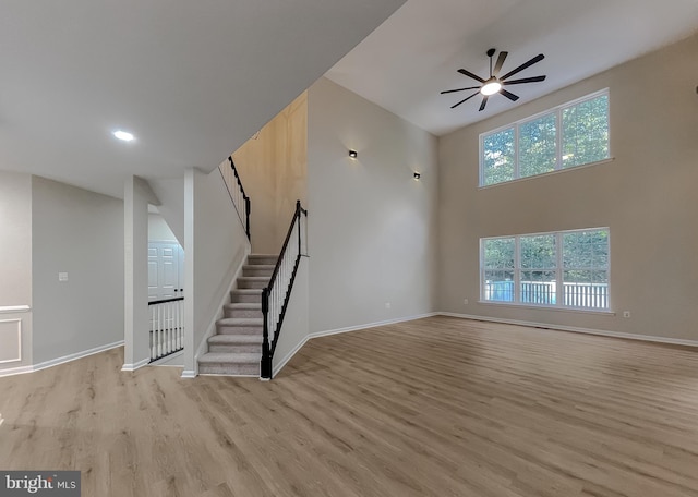 unfurnished living room with a towering ceiling, light hardwood / wood-style flooring, and ceiling fan