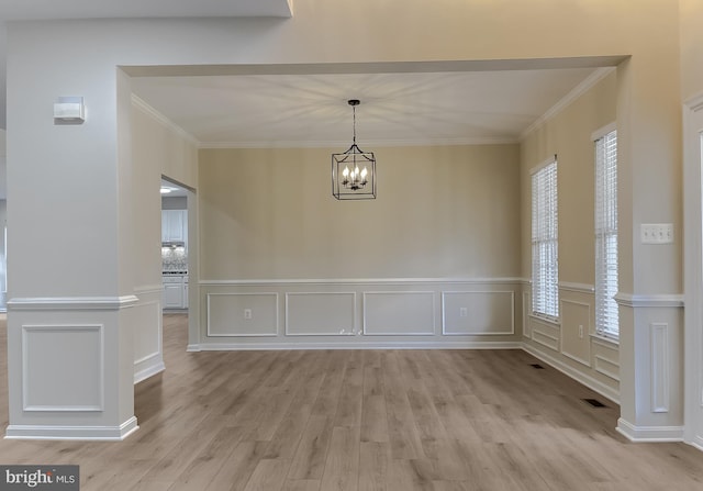 unfurnished dining area with crown molding, an inviting chandelier, and light wood-type flooring