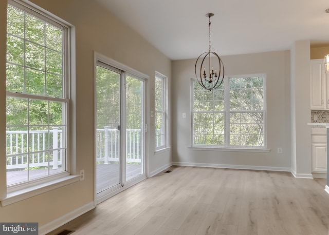 unfurnished dining area with a notable chandelier, a healthy amount of sunlight, and light hardwood / wood-style floors