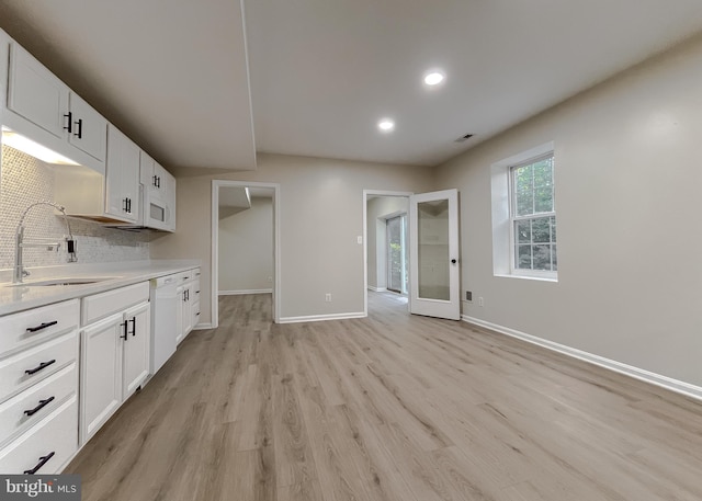 kitchen featuring decorative backsplash, white dishwasher, sink, light wood-type flooring, and white cabinets