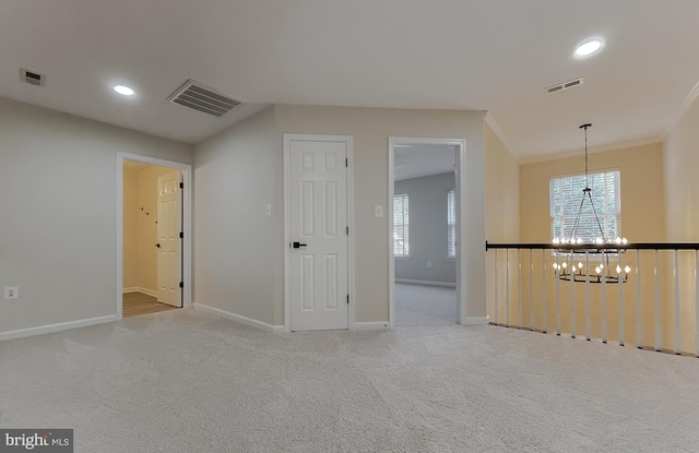 spare room with light carpet, ornamental molding, and a chandelier