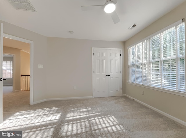 unfurnished bedroom featuring light carpet, multiple windows, a closet, and ceiling fan