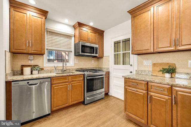 kitchen with light stone counters, backsplash, appliances with stainless steel finishes, light wood-type flooring, and sink