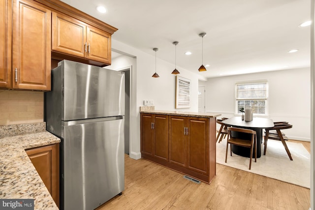 kitchen with decorative backsplash, light stone countertops, pendant lighting, light wood-type flooring, and stainless steel refrigerator