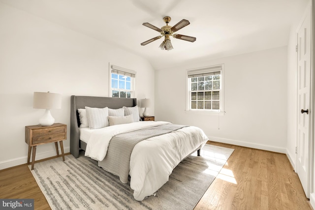 bedroom with light hardwood / wood-style floors, vaulted ceiling, multiple windows, and ceiling fan