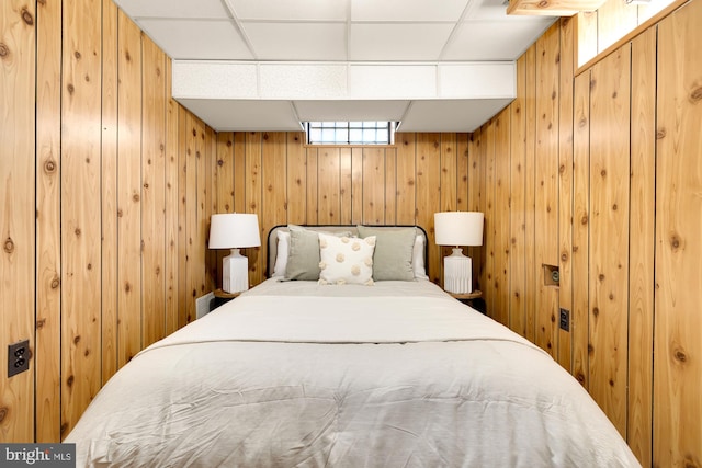 bedroom featuring a drop ceiling and wooden walls