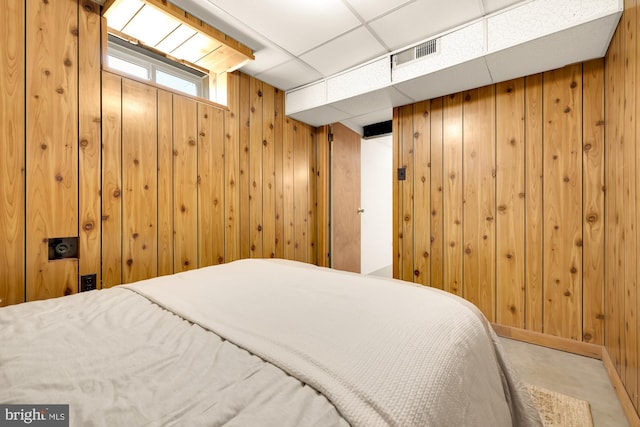 bedroom featuring a drop ceiling, wood walls, and concrete flooring