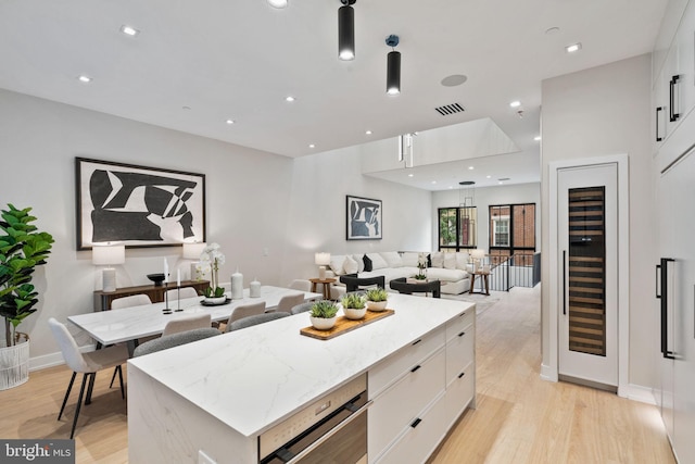 kitchen featuring light stone counters, white cabinets, beverage cooler, a center island, and light hardwood / wood-style floors