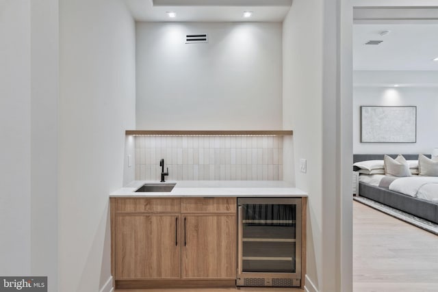 bar featuring wine cooler, light hardwood / wood-style flooring, and sink