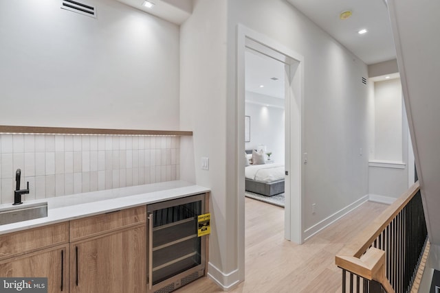 bar featuring light wood-type flooring, beverage cooler, and sink