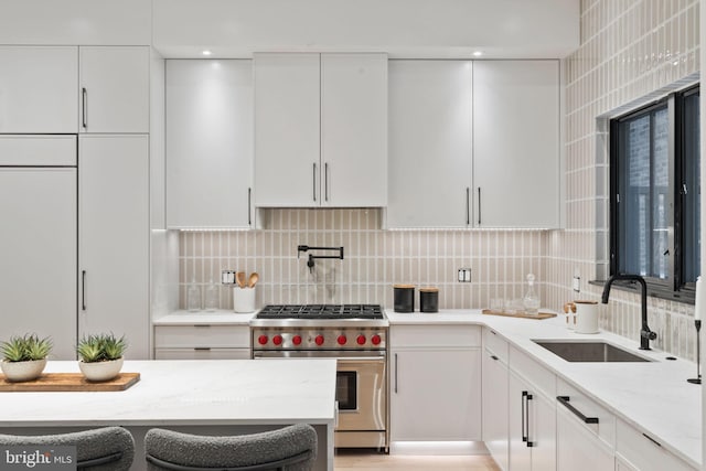 kitchen featuring tasteful backsplash, premium stove, light stone counters, sink, and white cabinets